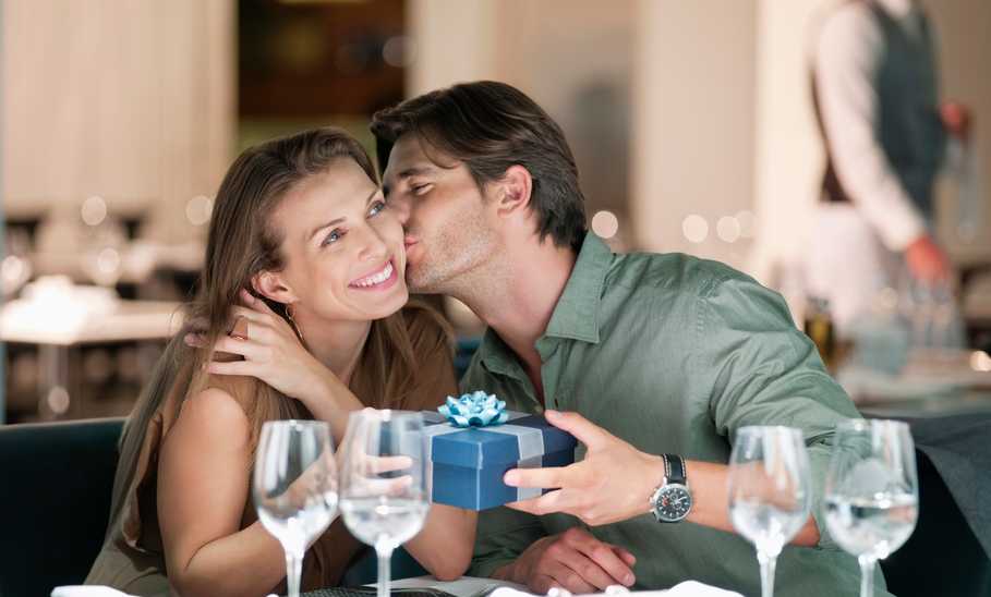 Man kissing and giving gift to woman in restaurant