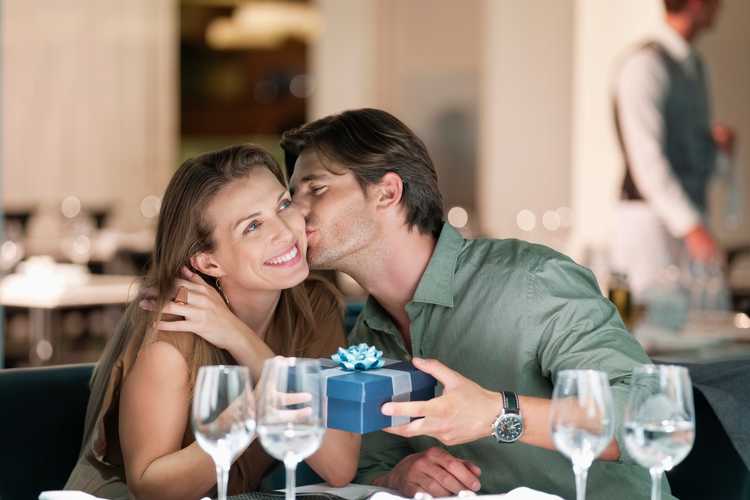 Man kissing and giving gift to woman in restaurant